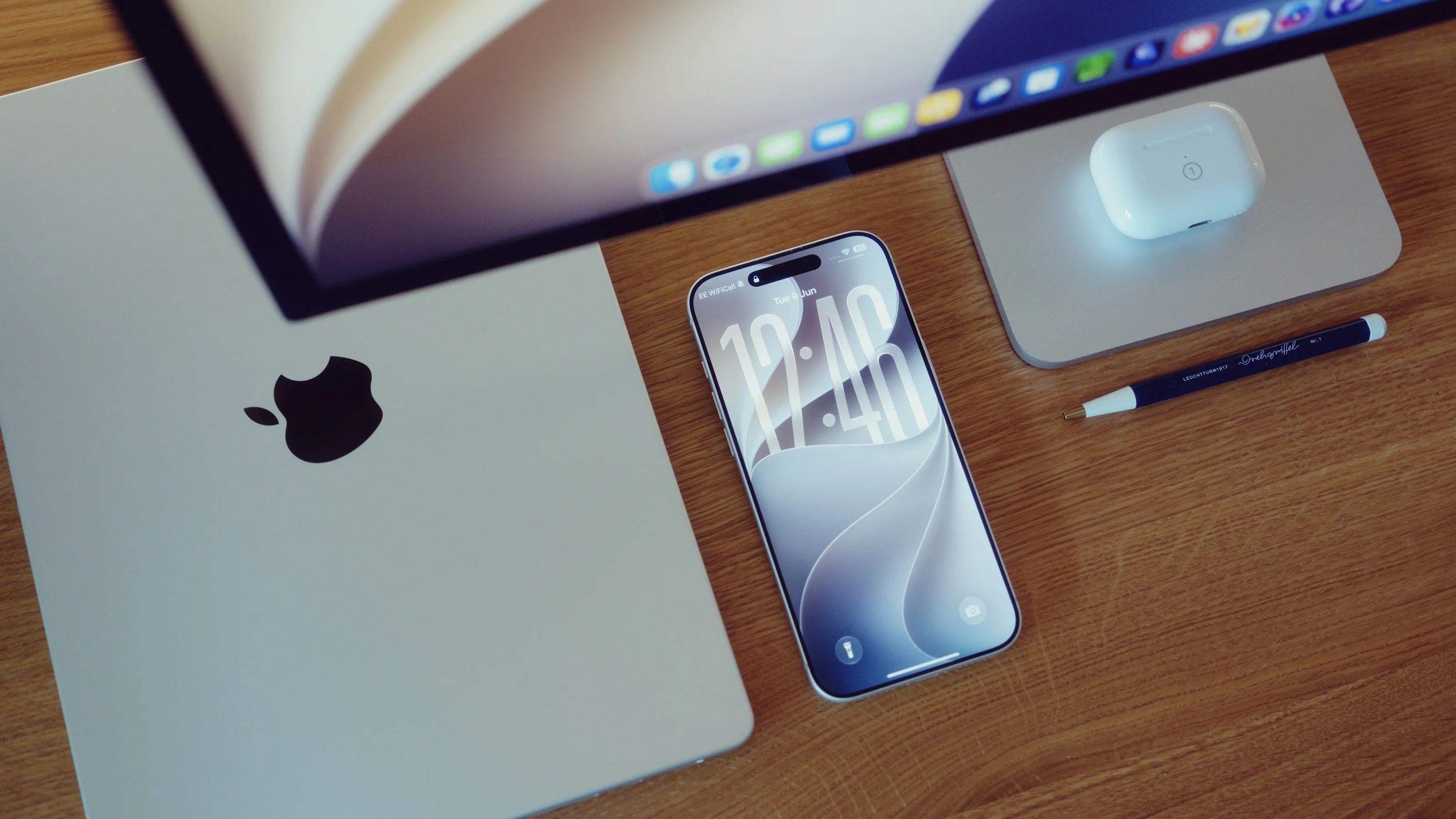 A laptop, phone, earbuds and an external display on a wooden desk, seen from above
