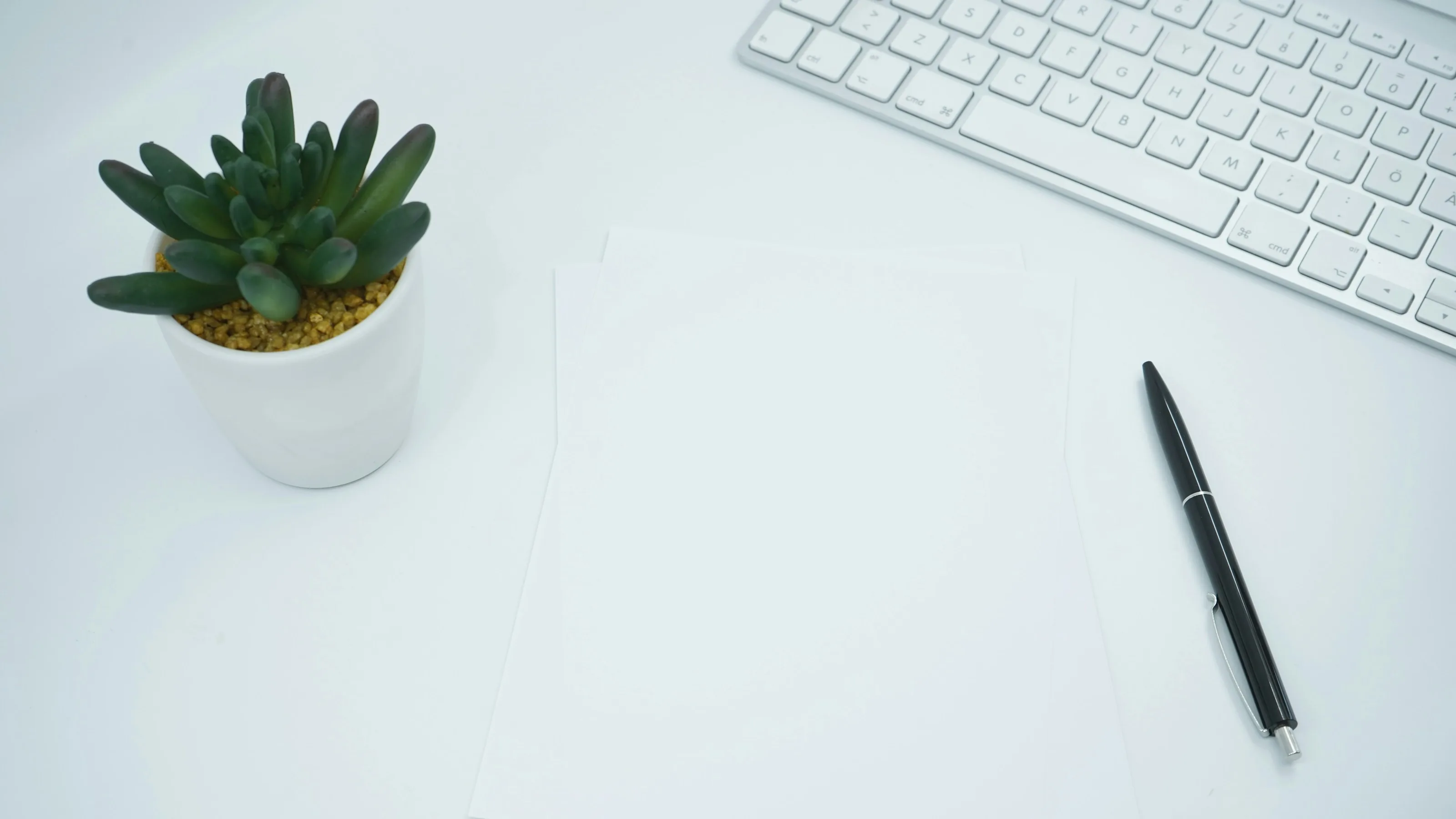A blank sheet of paper, a pen and a keyboard on a desk