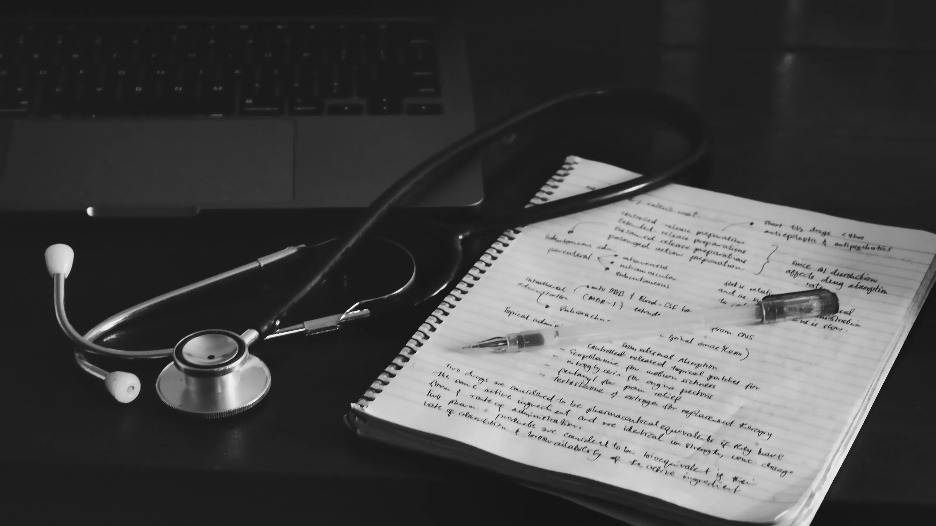 A stethoscope resting on a notebook beside a laptop